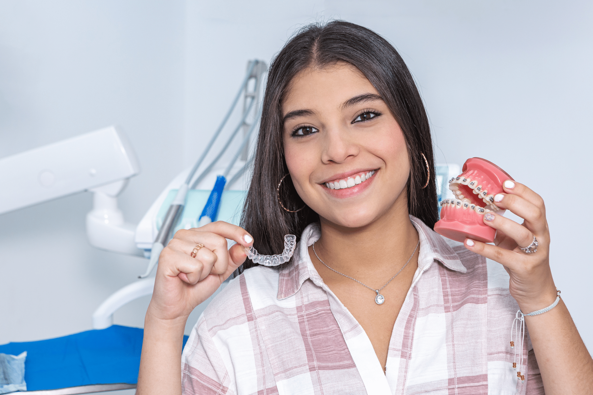 Smiling woman holding a clear aligner and a dental model with braces
